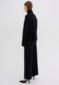 Black turtleneck sweater and wide-leg pants set, made from soft material. Features long sleeves and a relaxed fit, paired with pointed heels.
