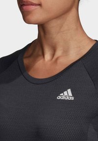 Detailní záběr na osobu, která má na sobě černé sportovní tričko Adidas s logem Adidas na horní části hrudníku.
