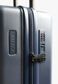 Maleta rígida de color azul marino con superficie texturizada, doble cremallera, cerradura integrada y un logotipo grabado en el lateral. Diseño compacto y duradero.