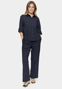 Navy blue blouse with a button-down front and rolled sleeves, paired with loose-fitting navy trousers and flat sandals.