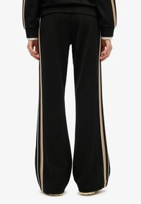 Sorte sweatpants med brede ben, lavet af blødt stof, med beige sidestriber og ribbede manchetter for et sporty look.