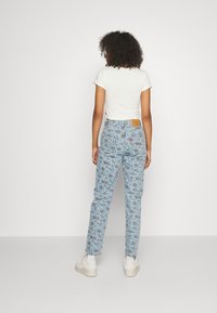 Jeans de cintura alta de color azul claro con un patrón floral, fabricados en denim. Combinados con una blusa ajustada de manga corta blanca y zapatillas blancas.