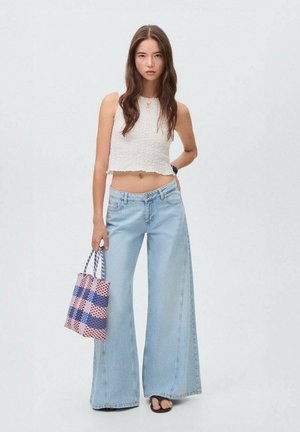 Lichtblauwe wijde jeans met een relaxte pasvorm, gecombineerd met een witte, cropped, gestructureerde tanktop en een geprinte totebag in roze en blauw.