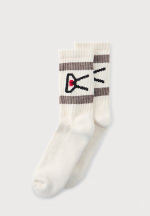 Paire de chaussettes blanches côtelées à tige mi-haute, avec des rayures grises et un logo noir et rouge, sur fond clair.