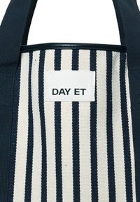 Gestreifte Canvas-Shopper-Tasche mit navyblauen und cremefarbenen vertikalen Streifen. Mit einem weißen Etikett mit dem Text "DAY ET". Stabile Griffe zum Tragen.