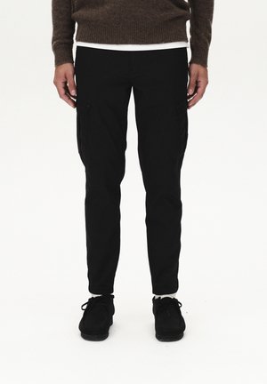 Black cargo pants featuring side pockets, a slim fit, and elastic cuffs, paired with black shoes and a brown textured sweater.