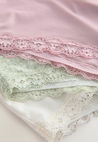 Vier gelaagde stofstukken: lichtroze, bleekgroen, wit en crème, elk met decoratieve kantafwerking in bijpassende kleuren.