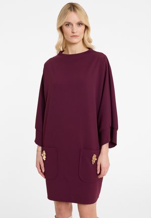 Maroon dress with a high neckline and wide sleeves. Features two front pockets with decorative golden accents. Smooth fabric texture.