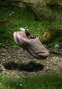 Chaussure slip-on marron clair avec une texture matelassée, un embout renforcé et une semelle en caoutchouc. Présente un design à trois bandes et une petite étiquette sur le talon.