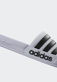Adidas slides med en lys lilla stropp, svart tre-stripes design, teksturert band og myk skumgummi såle for komfort.
