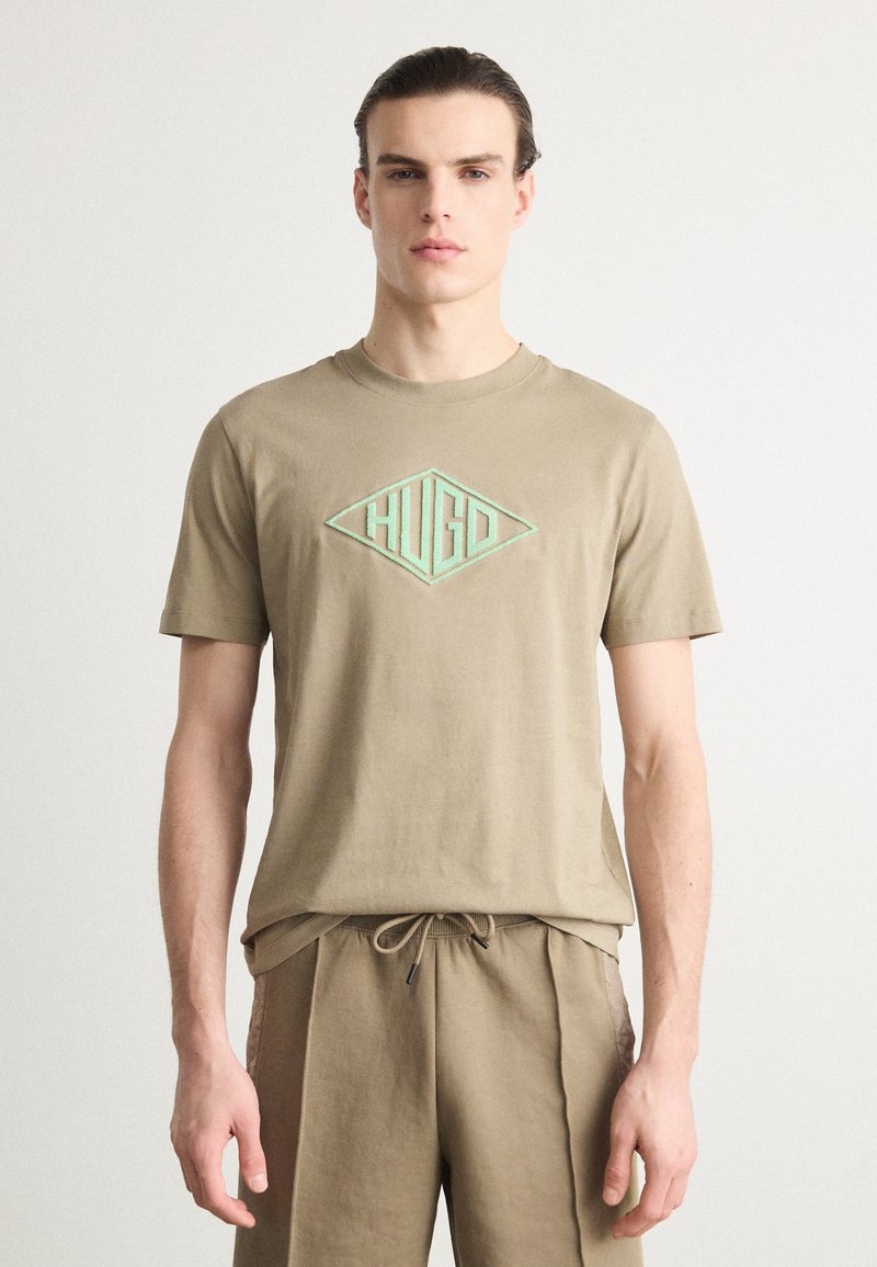 Kaki bomulls T-skjorte med rund hals, med et brodert mintgrønt diamantlogo i midten. Korte ermer.