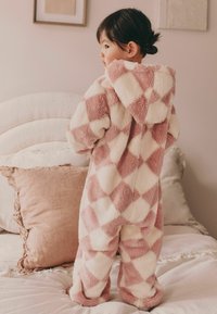 Salopetă pufoasă roz și albă cu model în romb, cu glugă, având o textură moale și o croială lejeră, purtată de un copil.