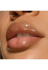 Lèvres brillantes, nude avec un subtil éclat. Texture douce, forme légèrement définie et une touche de brillance reflétant la lumière naturelle.