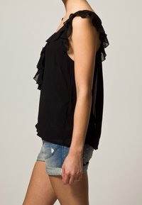 Svart ärmlös topp med volangdetaljer längs axlarna, kombinerad med denimshorts. Toppen har en flödande design och lättviktig tyg.