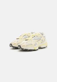 Lacoste tenisice od žutog mrežastog materijala s srebrnim detaljima i sivim gumenim potplatima. Imaju istaknuto vezivanje i podstavljen jezik za udobnost.