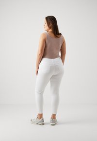 Top de tirantes a rayas en naranja y azul, combinado con unos jeans blancos ajustados. Los zapatos son deportivos en plata y gris, con cordones visibles y marca.