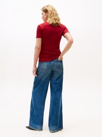 Camiseta corta de manga roja combinada con pantalones vaqueros de denim azul de pierna ancha, que presentan una tela texturizada y costuras visibles en los dobladillos.