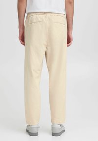 Beige elastiske bukser med to baklommer, rett ben-design og en glatt tekstur, kombinert med grå sneakers.