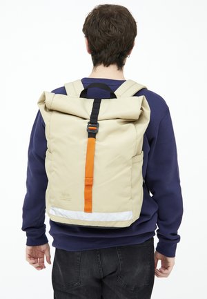 Beige rolrugzak met een oranje centrale strap, zwarte hardware en reflecterende accenten aan de basis. Textuurstof ontwerp.