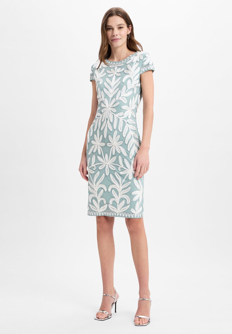 Kurzärmliges, knielanges Kleid in Hellblau mit weißer floralem Stickerei und gewelltem Saum; kombiniert mit silbernen Riemchen-Heels.