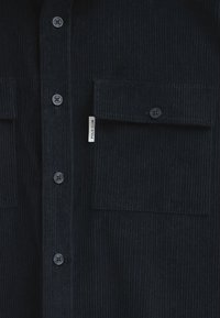 Camicia in corduroy blu scuro con abbottonatura frontale, due tasche sul petto e una piccola etichetta "POLO CLUB" di lato. Tessuto a coste strutturato.