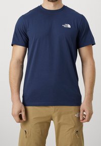 Navy blue short-sleeve t-shirt made of cotton, featuring a small white logo on the left chest. Crew neck design, smooth texture.