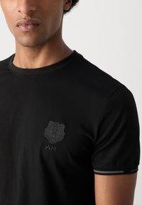 Zwarte T-shirt van gladde stof, met een getextureerde berenafbeelding op de borst en een subtiele gestreepte accent op de mouwzoom.