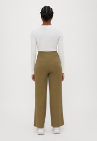 Long, straight-cut olive green pants with a ribbed texture and high waist, paired with a fitted white long-sleeve top. White sneakers visible.