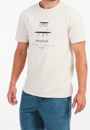 Mand iført hvid t-shirt med sort skateboardgrafik og tekst "PROTEST SPORTSWEAR EST. 93" kombineret med blå shorts.