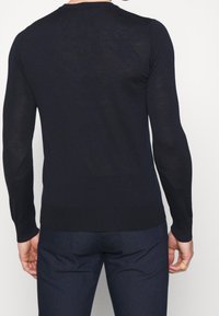 Marinblå stickad tröja med rund hals och långa ärmar, med en figursydd design och ribbat midjeband, sedd bakifrån.