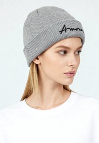 Grijze gebreide muts met geribbelde textuur en een omgeslagen boord, voorzien van zwarte scriptborduursel met de tekst "Amour".