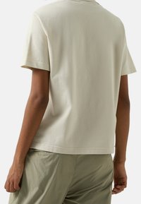 T-shirt en coton beige clair avec manches courtes, col rond et coupe décontractée. Le dos présente une texture lisse et des coutures minimales.