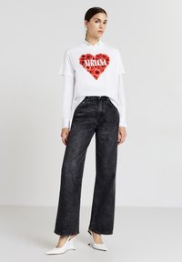 Maglietta bianca a maniche corte con grafica a forma di cuore floreale rossa e testo "NIRVANA", abbinata a jeans neri a vita alta e larghi e scarpe bianche.
