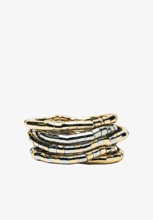 Stos elastycznych metalowych pierścieni z naprzemiennymi złotymi i srebrnymi segmentami na białym tle.