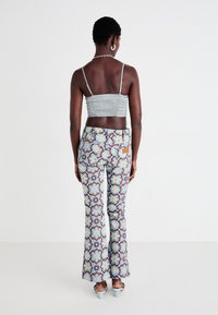 Sivý zavinovacíCrop top v kombinácii s vysokými rozšírenými nohavicami s modrým kvetinovým vzorom a svetlohnedými akcentmi; hladká textúra.