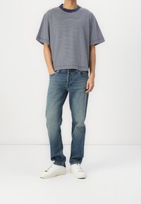 Camiseta a rayas en azul marino y blanco con cuello redondo, combinada con jeans de mezclilla azul claro y zapatillas blancas. Ajuste y apariencia casual.