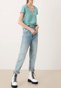 Türkisfarbenes V-Ausschnitt-T-Shirt, leicht locker geschnitten, kombiniert mit hochtaillierten, hellblauen Jeans. Abgerundet wird der Look durch weiße Schnürkampfstiefel.
