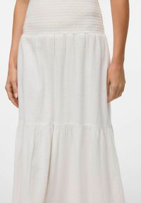 Robe maxi blanche avec un corsage smocké, une jupe évasée à plusieurs niveaux, et un tissu léger et texturé. Fini lisse avec un éclat subtil.