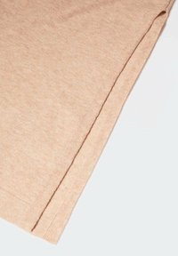 Tissu tricoté beige avec un détail de bord plié, présenté sur un fond clair uni.