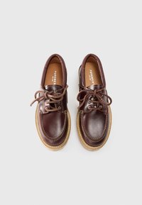 Zapatos de cuero marrón con punta redonda, cordones en la parte frontal y detalles cosidos. Presenta una suela de goma ligera en tono beige y un acabado suave.
