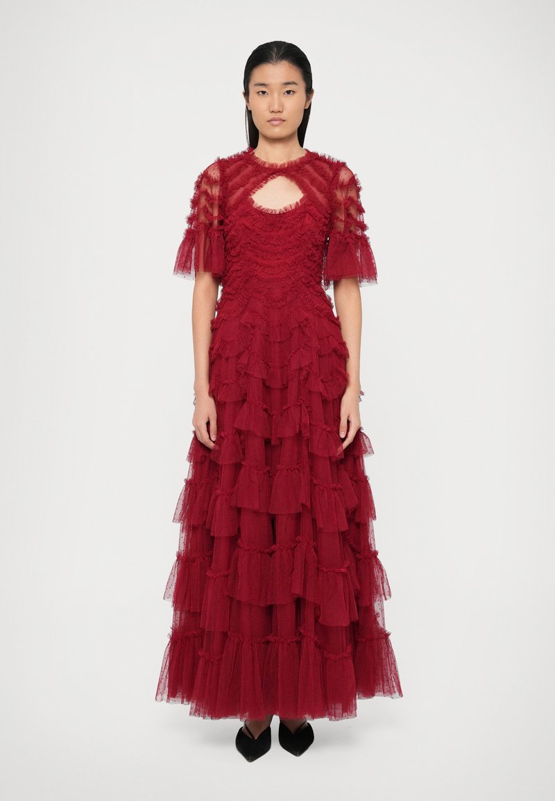 Raudona maxi suknelė su sluoksniais, pagaminta iš permatomo tiulio, su raukšlėmis, raktelio forma iškirptėje ir trumpomis pūstomis rankovėmis.