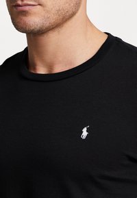 Svart bomull T-skjorte med rund hals. Har en liten hvit polo-spiller logo på brystet. Minimalistisk design og glatt tekstur.