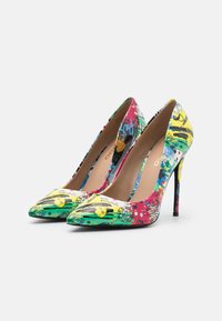 Une paire d'escarpins à bout pointu avec un design style graffiti multicolore, présentant des accents jaunes, verts, rouges, bleus et noirs sur un fond blanc.