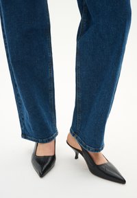 Schwarze Leder-Pumps mit spitzem Schnitt und schlanken Absätzen, kombiniert mit blauen Jeans mit geradem Bein und kontrastierenden gelben Nähten.