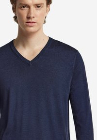 Marinblå långärmad v-ringad tröja, gjord av ett slätt, strukturerat tyg, med en ren halsringning och figurnära silhuett.