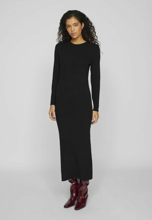 Black knitted dress with long sleeves, crew neckline, and a fitted silhouette. Worn with shiny burgundy knee-high boots.