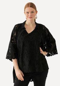 Top de encaje negro con un collar tipo camisa abotonado, escote en V y mangas acampanadas con intrincados patrones florales y bordes con forma de olas.