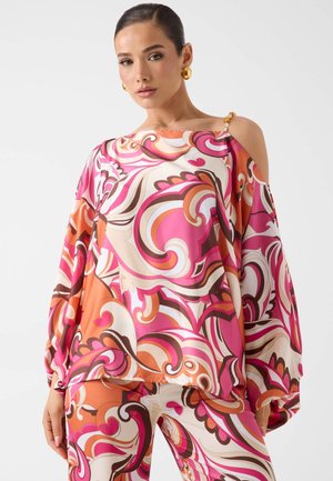 Femme portant une tenue à motif abstrait tourbillonnant rose vif, orange et blanc avec une découpe asymétrique à une épaule et des boucles d'oreilles anneaux dorés.