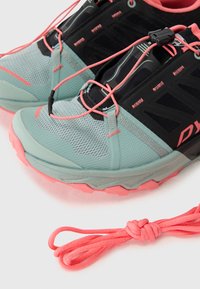 Athletic shoes in mint green with black and pink accents; mesh material, thick textured sole, elastic laces, and notable design patterns.