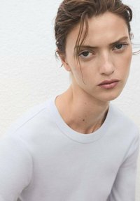 Himmelblaues Langarmshirt mit rundem Ausschnitt, weicher Textur und minimalen Nähten. Der Stoff wirkt glatt und leicht körpernah.